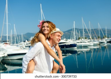 Attractive young couple walking alongside the marina with moored boats on a luxury waterfront in summer sunshine