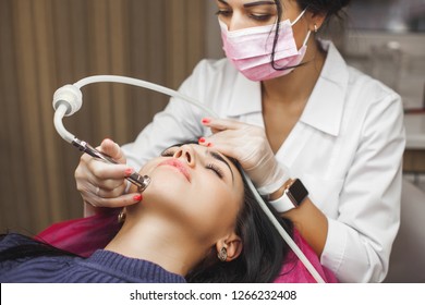 Attractive Young Doctor Making Mesotherapy To Her Client. Woman In The Beauty Salon. Doctor Making Face Treatment With Medical Apparatus. Diamond Skin Peeling Procedure In The Clinic.