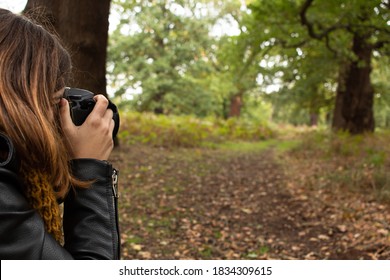 Attractive Young Female With A Black Leather Jacket Taking A Photo With Her Reflex Camera While Walking On The Park During Autumn