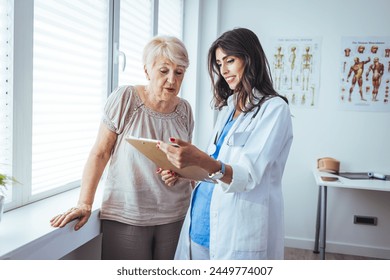 Attractive young female doctor consulting with a patient inside her office at a hospital. Close up of a senior woman having a doctors appointment. A female doctor standing next to female patient  - Powered by Shutterstock