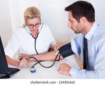 Attractive Young Female Doctor Or Nurse Taking A Male Patients Blood Pressure Using A Sphygmomanometer