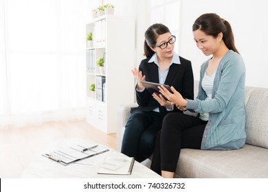 Attractive Young Female Insurance Agent Using Mobile Pad Computer Showing Invest Document For Smiling Girl And Explaining Plan.