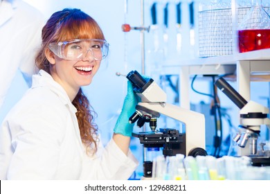 Attractive Young Female Research Science Student Having Fun Looking At The Microscope Slide In The Life Science (forensics, Microbiology, Biochemistry, Genetics, Oncology...)laboratory.