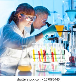 Attractive Young Female Scientist And Her Senior Male Supervisor Pipetting And Microscoping In The Life Science Research Laboratory (biochemistry, Genetics, Forensics, Microbiology..)