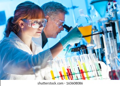 Attractive Young Female Scientist And Her Senior Male Supervisor Pipetting And Microscoping In The Life Science Research Laboratory (biochemistry, Genetics, Forensics, Microbiology..)