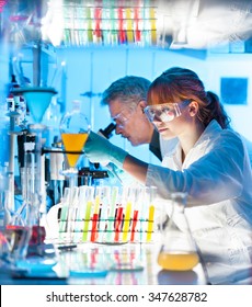 Attractive Young Female Scientist And Her Senior Male Supervisor Looking At The Cell Colony Grown In The Petri Dish In The Life Science Research Laboratory