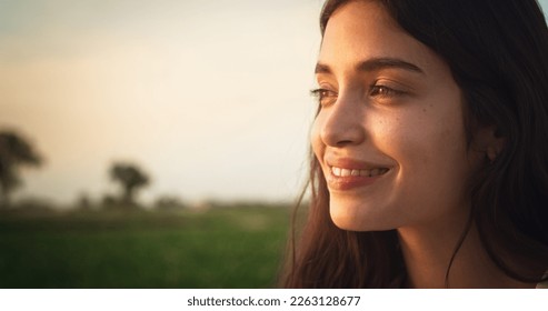 Attractive Young Female Standing Outdoors and Enjoying Nature Around. Smiling Brunette Girl with Natural Face Features and Green Eyes. Scenic Sunset Light and a Cinematic Rural Landscape. Close Up - Powered by Shutterstock