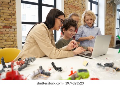 Attractive Young Female Teacher In Glasses Showing Scientific Robotics Video To Curious Kids Using Laptop During STEM Class