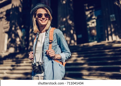 Attractive young female tourist is exploring new city. Woman with retro camera in search of new adventures.