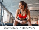 Attractive young fit sportswoman resting after exercises while sitting in the gym