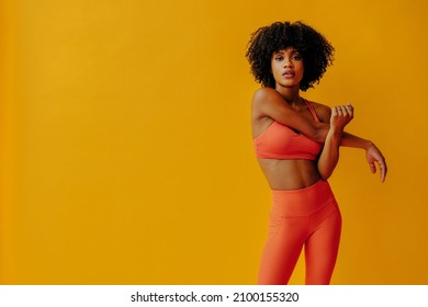 attractive young fit woman in sportswear stretching isolated on orange background 