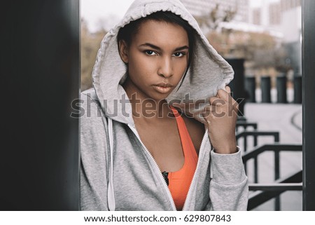 Attractive young fitness woman in sportswear wearing hood and posing on stadium