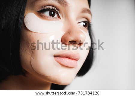 An attractive young girl with black hair, with silicone patches on her face, moisturizes the skin