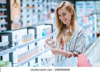 Attractive young girl is doing shopping with shopping bags in perfume store in modern mall.