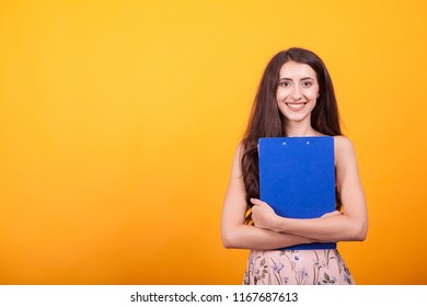 Attractive young girl holding blue clipboard in studio over yellow background. Successful young woman - Shutterstock ID 1167687613