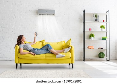 attractive young girl lying on yellow sofa under air conditioner at home