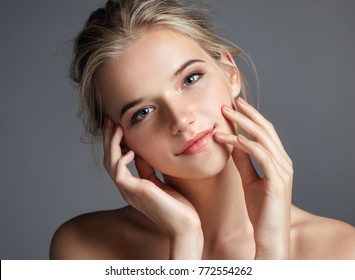 Attractive young girl touching her lips. Photo of blonde girl with perfect skin on grey background. Beauty & Skin care concept