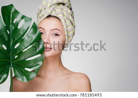 attractive young girl with a towel on her head, with clean skin on her face, holds a green leaf, day spa