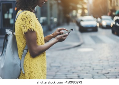 Attractive young girl walking in the city and using an app on smartphone, side view of hipster girl traveling and sending message via her cellphone, sunset in the background