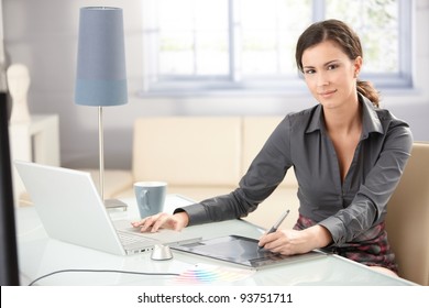 Attractive Young Graphic Designer Using Laptop And Tablet, Working At Home, Smiling.?