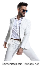 Attractive Young Guy In White Suit With Retro Sunglasses Looking To Side And Posing In A Fashion Studio Light On White Background 