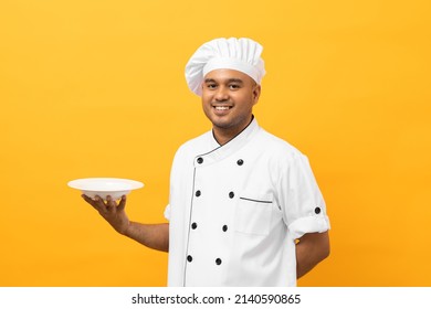 Atractivo joven y apuesto chef asiático uniformado que sostiene un plato vacío delicioso menú de buen gusto aislado. Cocinando al hombre indio El chef de la ocupación o la panadería People en el restaurante y el hotel de la cocina.