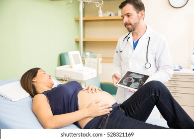 Attractive Young Hispanic Doctor Showing An Ultrasound Image To A Pregnant Patient And Giving Her Some Serious News