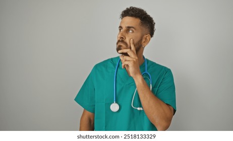 Attractive young hispanic male nurse in green scrubs with a stethoscope around his neck, posing thoughtfully against an isolated white background. - Powered by Shutterstock