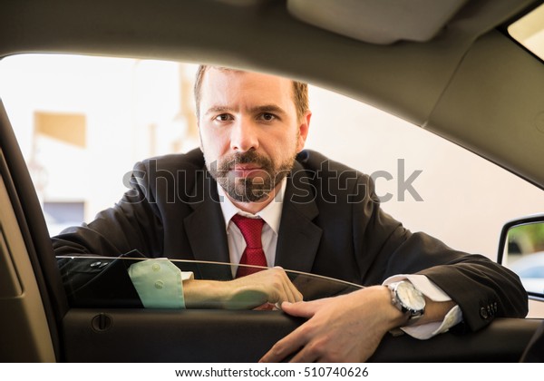 Attractive young Hispanic salesman in a suit leaning\
on a car door and selling\
cars