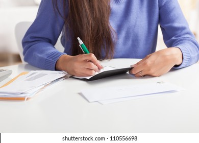 Attractive Young Hispanic Woman Sitting At Table Paying Bills And Doing Banking Wearing Blue Sweater.