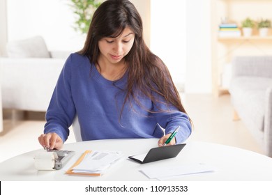 Attractive Young Hispanic Woman Sitting At Table Paying Bills And Doing Banking Wearing Blue Sweater.