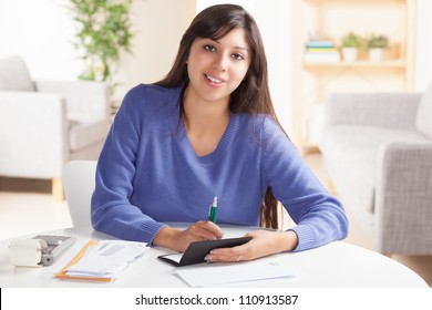 Attractive Young Hispanic Woman Sitting At Table Paying Bills And Doing Banking Wearing Blue Sweater.