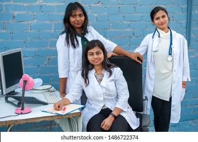 Attractive young Indian college students study abroad at prestigious institute. Successful girls in white coats with computer posing in front of camera with teaching professor. Stethoscope, laptop