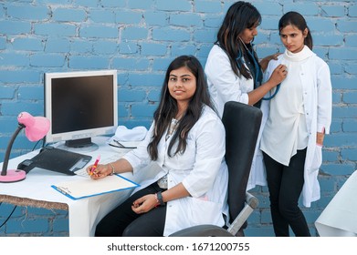 Attractive young Indian college students study abroad at prestigious institute. Successful girls in white coats with computer posing in front of camera with teaching professor. Stethoscope, laptop