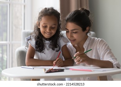 Attractive young Indian mother   little daughter drawing pictures in paper and colored pencils  Loving family enjoy communication   common creative hobby spend leisure at home  Artistic pastime