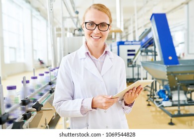 Attractive Young Inspector Wearing White Coat Looking At Camera With Charming Smile While Standing At Spacious Soy Milk Factory With Digital Tablet In Hands, Waist-up Portrait Shot