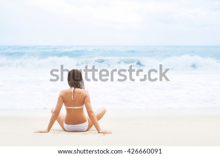 Attractive, young lady sitting on the beach and enjoying the scene of wavy sea.