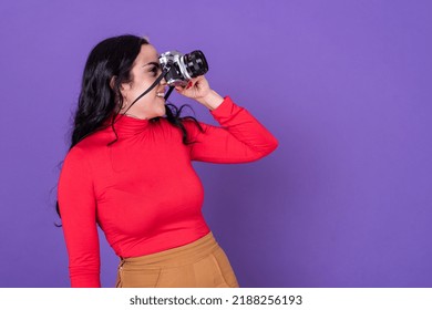 Attractive Young Lady Taking A Photo With Her Film Camera Over A Violet Background. Copy Space. Studio Shot.