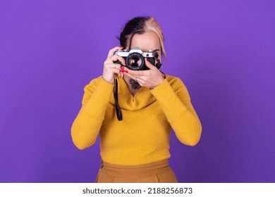 Attractive Young Lady Taking A Photo With Her Film Camera Over A Violet Background.  Studio Shot.