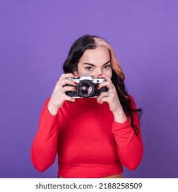 Attractive Young Lady Taking A Photo With Her Film Camera Over A Violet Background.  Studio Shot.