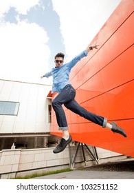 Attractive Young Male Model Jumping Outdoors In Blue Shirt And Sunglasses