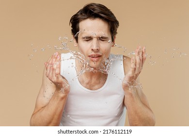 Attractive Young Man 20s Perfect Skin In Undershirt Surrounded By Water Drops Wash His Face Isolated On Plain Pastel Beige Background Studio Portrait. Skin Care Healthcare Cosmetic Procedures Concept