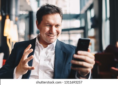Attractive young man in a bar getting good results over an email on his mobile phone. He is celebrating by raising his hand in the air. - Shutterstock ID 1311693257