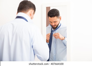 Attractive Young Man With A Beard Getting Dressed And Tying A Knot On A Necktie At Home