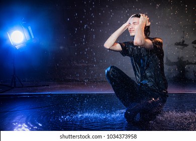 Attractive Young Man In Black Wet Clothes Under The Rain And Splash Of Water During Studio Photo Shoot