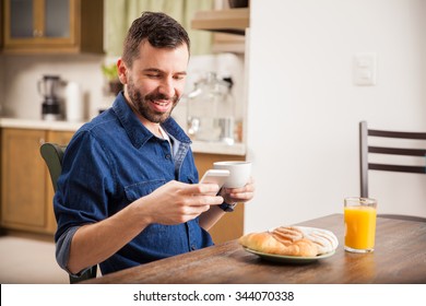 Attractive young man in denim shirt texting on his smartphone while having breakfast at home - Powered by Shutterstock