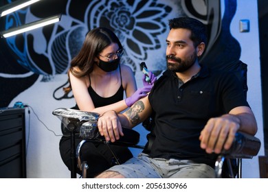 Attractive young man getting a new tattoo on his arm. Alternative customer with a nose piercing at the ink studio - Powered by Shutterstock