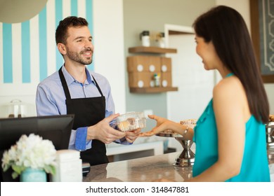 Attractive Young Man Handing Over A Box With Pastries To A Customer In A Cake Shop And Smiling