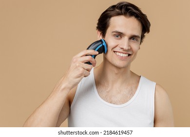 Attractive Young Man He 20s Perfect Skin In Undershirt Hold Electric Razor Shaving Trimming Isolated On Plain Pastel Beige Background Studio Portrait. Skin Care Healthcare Cosmetic Procedures Concept