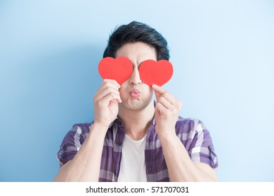 Attractive young man holding red love hearts over eyes isolated on blue background